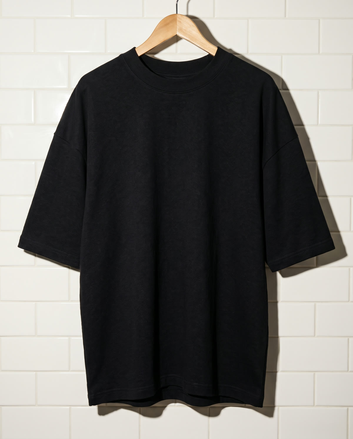 Black heavyweight boxy tee on a wooden hanger against white tile.